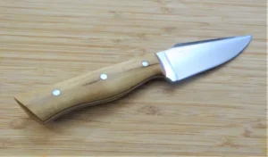 Right side of Palatka Holly Harpoon Clip Point Knife showcasing 1095 blade and mild steel pins on wooden surface