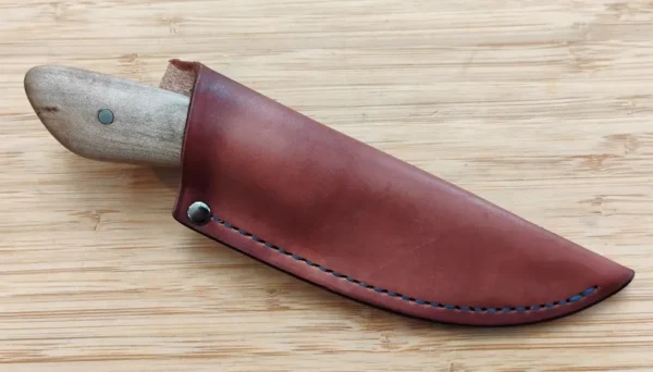 Red Maple Goldilocks #217 knife in a custom hand-cut leather sheath, on a wooden surface.