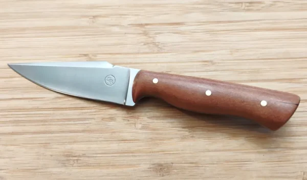 Full left view of Wild Black Cherry Harpoon Clip Point #343 high carbon steel knife with brass pins on a wooden surface.