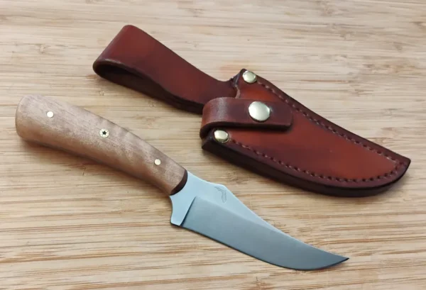 South Florida Black Olive Trailing Point #311 knife next to a custom leather sheath, displayed on a bamboo cutting board.