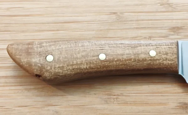 Closeup of the right side on Pecan Brisket Knife #348 handle with showing unique grain structure on a wooden surface