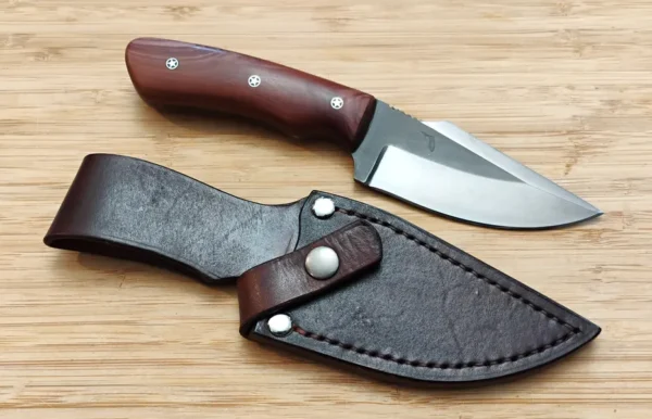 Red Cedar Chubby #353 custom knife placed beside its custom veg-tanned leather sheath on a wooden surface.